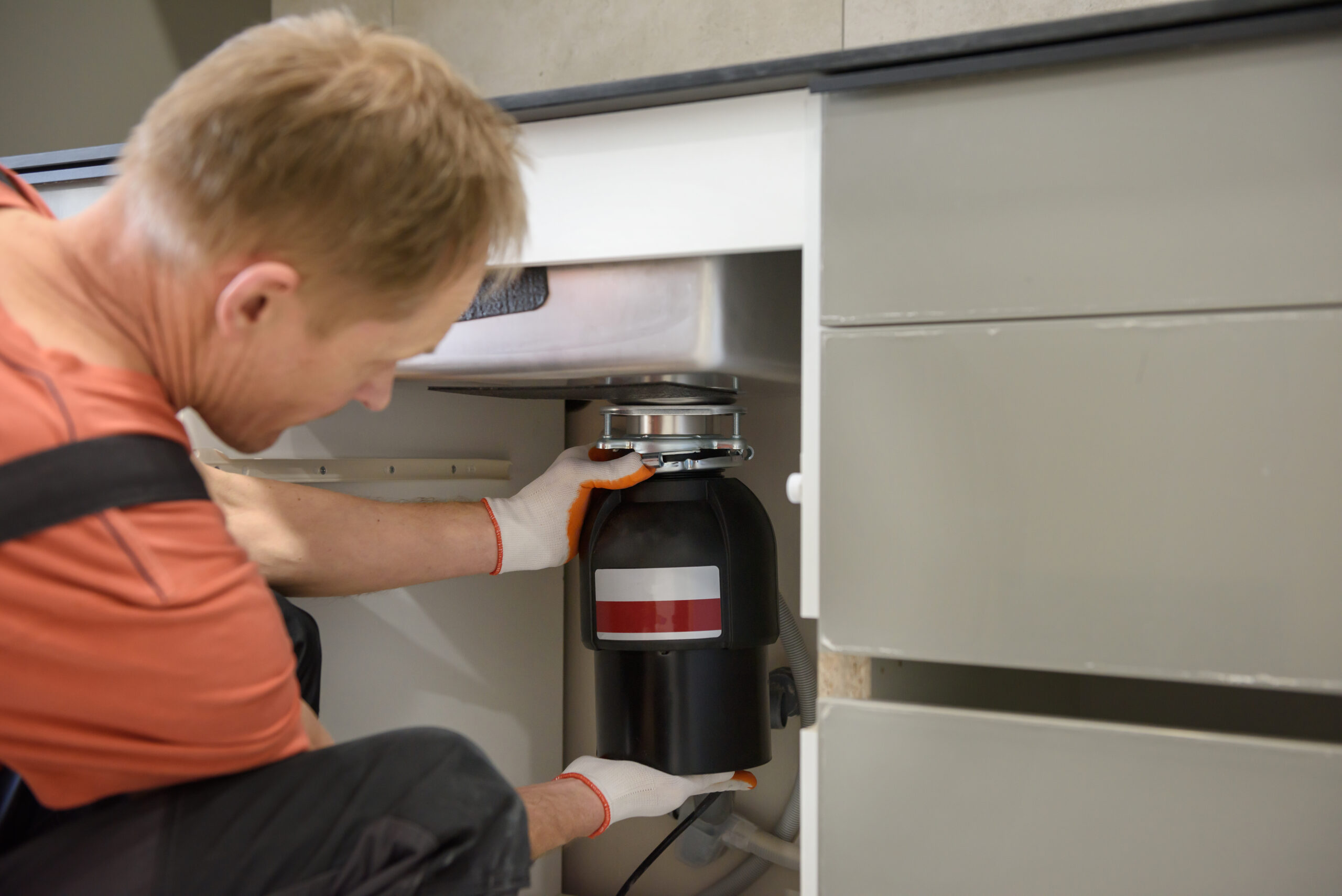 The worker is installing a household waste shredder for the kitchen sink.